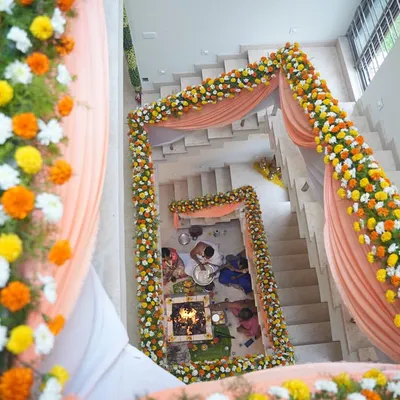 An aerial view of a housewarming ceremony (Griha Pravesh) setup. We created a mandap around the staircase using marigold garlands and drapes, transforming the home's interior for the puja.