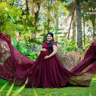 This wide-angle shot captures the full splendor of a flowing maroon maternity gown in a lush, green paradise. The fabric seems to dance in the air, creating a truly breathtaking image.