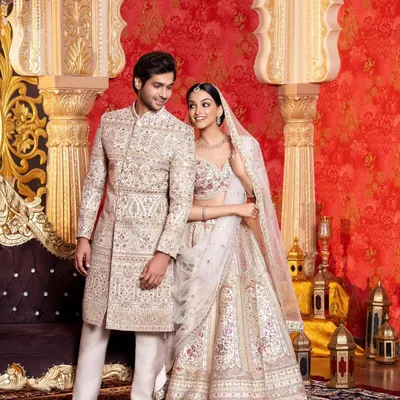 A stunning example of wedding day coordination. The bride and groom are dressed in matching ivory and gold outfits, with her lehenga and his sherwani featuring identical intricate embroidery, creating a seamless and royal look.