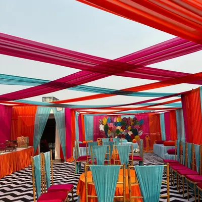 A stunningly vibrant Mehendi setup with a canopy of pink, orange, and turquoise drapes. The chevron-patterned floor and colorful seating created a lively and festive atmosphere.