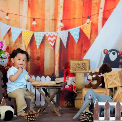 A one-year-old enjoying our rustic wood cafe theme, sitting at a small table in a cozy, camp-like setting with string lights and stuffed animals.
