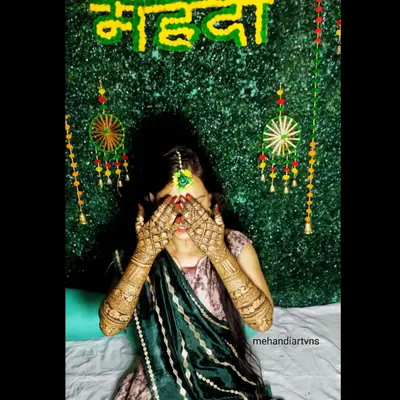 A classic shy bride pose behind her beautifully decorated hands. The green background makes the rich color of the mehandi stand out.