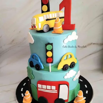 A fun two-tier transport cake for a first birthday. The design features a road, traffic lights, and cute, colorful cars and buses that little ones love.