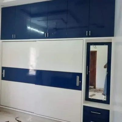 A floor-to-ceiling wardrobe with a bold blue and white high-gloss finish. This design combines sliding doors for the main section with a separate dressing mirror unit and upper loft cabinets for extra storage.