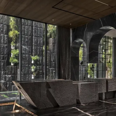 This super-luxury home is a perfect blend of opulent architecture and nature. A monolithic stone bar stands before a full-height window looking out onto a vertical garden, all reflected in the polished black marble floor. This is sustainability at its most luxurious.