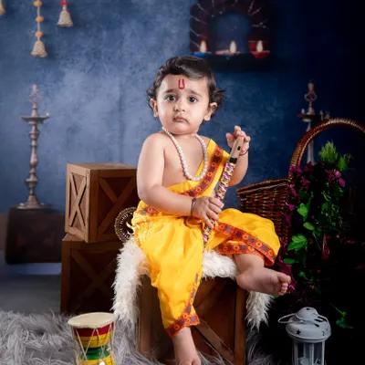 A classic studio portrait for Janmashtami, with a baby boy dressed as Lord Krishna. We use professional lighting and a carefully arranged set with props like a flute and dholak to create a divine and adorable scene.