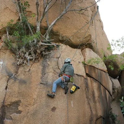 The hard work behind the send. Here, a team member is equipped for route development, a process that involves cleaning the rock and installing permanent safety anchors to create new climbs for the community.