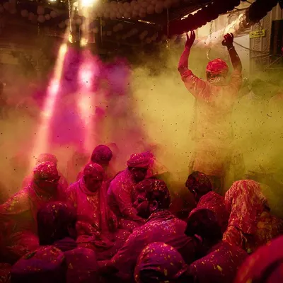 Inside a temple during Barsana Holi, where clouds of pink and yellow gulal fill the air. A single ray of light illuminates the scene of joyful celebration.