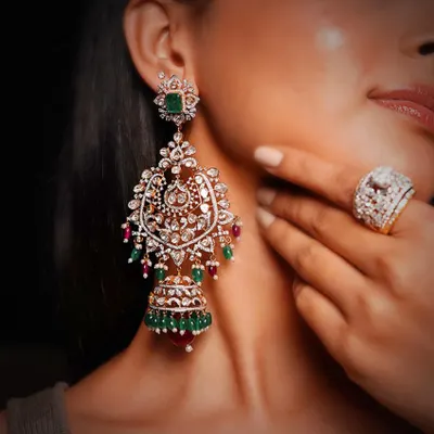 A pair of magnificent bridal earrings, combining traditional jhumka and chandelier styles. The piece features Polki diamonds, vibrant emeralds and rubies, and intricate enamel work, making it a true heirloom.