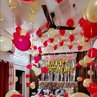 A classic birthday room decoration with red and cream balloons filling the entire space. The setup includes a silver foil curtain behind the bed and 'Happy Birthday' foil balloons to create a festive atmosphere.
