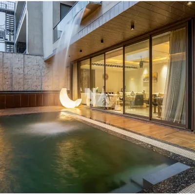 The poolside deck at dusk, where the space transforms into an intimate setting for evening gatherings. The cascading waterfall and illuminated moon sculpture add a touch of magic, reflecting beautifully on the water's surface.