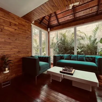 An interior view of a stunning patio room at Zonasha Paradiso for Mr. Amar Nagaram, founder of Virgio. This space features rich Brazilian Ipe wood flooring, wood-paneled walls, and a Mangalore tile roof, furnished with elegant teal sofas for a luxurious feel.