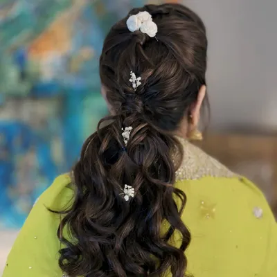 A detailed view of a chic and intricate ponytail. This hairstyle features woven sections and soft curls, adorned with small floral accessories, making it a perfect choice for a Mehendi or Sangeet ceremony.