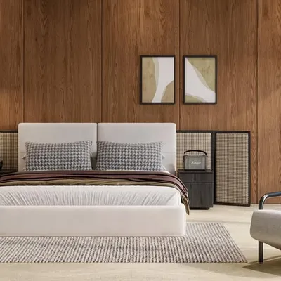 This minimal bedroom design focuses on creating a sense of calm. The warm wood-paneled accent wall, low-profile bed, and simple armchair are arranged to feel uncluttered and serene, with large windows letting in abundant natural light.