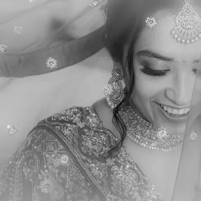 A soft and dreamy black and white portrait. The bride's joyful, shy smile is captured through her delicate veil, creating a moment of pure, understated beauty.