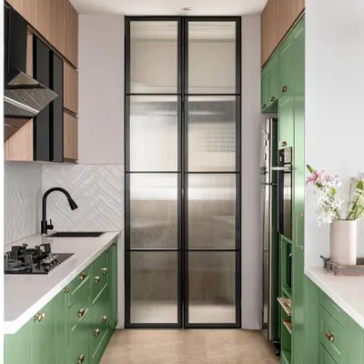 A full view of our Elle Decor-featured kitchen. This galley layout includes a utility area separated by a fluted glass door, built-in appliances, and a beautiful contrast between the green cabinets and wood-tone overheads.