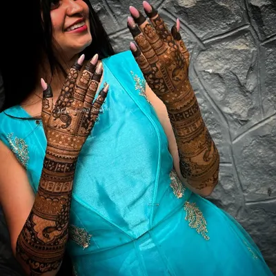 A happy engagement bride showing off her beautifully stained mehendi. The deep brown color looks stunning against her blue dress.