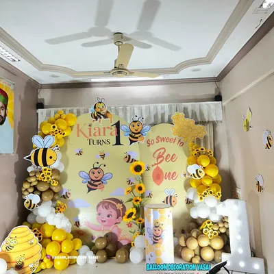 A "So Sweet to Bee One" theme for Kiara's first birthday. This setup features a custom backdrop with cute bumblebee characters, a yellow and white balloon arch, and a large light-up number one.