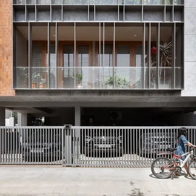 The ground level of 'Triode' shows the sleek louver system that provides privacy for the first-floor apartment while maintaining a visual connection to the street. The elevated structure also allows for sheltered parking underneath.