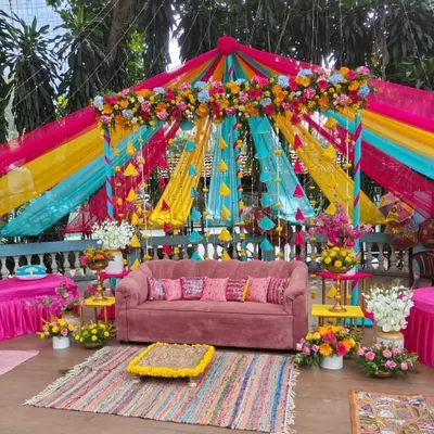 A spectacular Mehendi setup featuring a canopy of vibrant drapes in pink, yellow, and turquoise. The colorful theme is perfect for a lively and joyful daytime celebration.