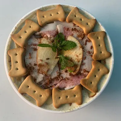 A close-up of my Apple & Bacon Pup Scoops. This dog-friendly ice cream is made with real ingredients, garnished with fresh apple, mint, and crunchy biscuits. It's a gourmet treat that's both delicious and healthy for your pup.