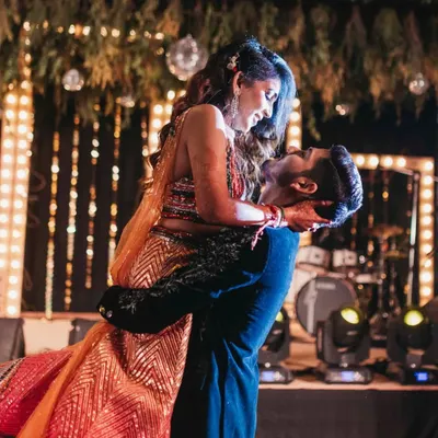 A classic romantic lift on the dance floor during the couple's Sangeet performance. This shot captures the chemistry and joy between the couple against a backdrop of stage lights.
