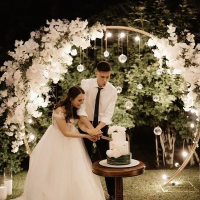 A romantic moment during an outdoor evening engagement. I created a beautiful circular arch with white flowers and hanging glass globes with lights to frame the cake-cutting ceremony.