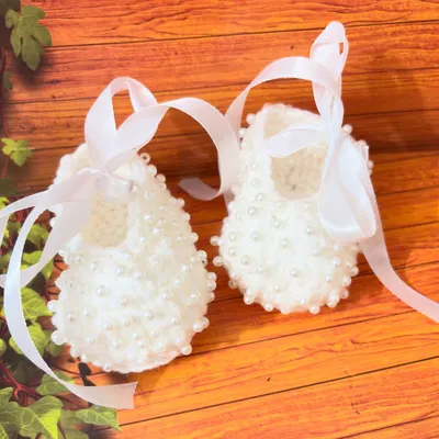 These beautiful white booties are adorned with dozens of tiny pearls and finished with a soft satin ribbon, making them a truly special choice for a baptism.