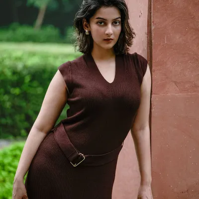 A powerful outdoor portrait of a model in a form-fitting brown dress, leaning against a wall. The pose and direct gaze create a confident and striking image.