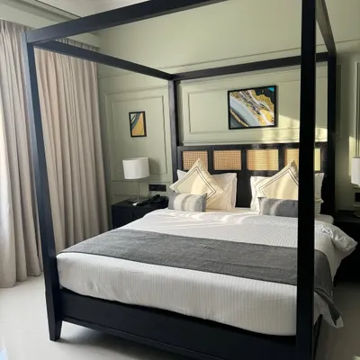 A modern four-poster canopy bed with a clean, minimalist frame in a black finish. The headboard features teak and cane panels, combining modern and traditional elements. This was part of a hotel project.