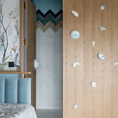 A peek into a child's dream bedroom. The design seamlessly integrates a rock-climbing wall that doubles as a wardrobe door, leading to a bathroom with a playful chevron tile pattern.