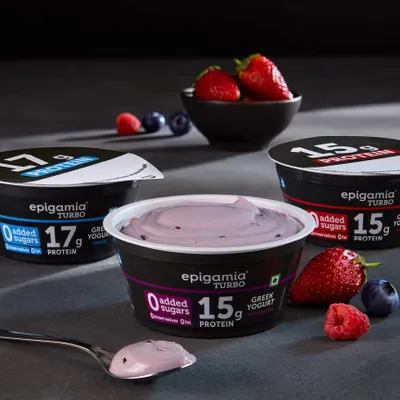 A clean product shot of Epigamia's Turbo protein yogurts. The focus here is on the creamy texture of the yogurt on the spoon and the fresh berry ingredients, communicating both taste and health.