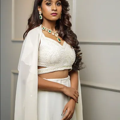This all-white Indo-Western outfit features a beautifully textured crop top, a simple skirt, and a sheer, floor-length cape for a touch of drama.