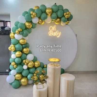 A modern and chic baby shower decoration with a sage green, white, and gold balloon arch. The "Oh Baby" neon sign on a clean white backdrop creates a beautiful photo corner.