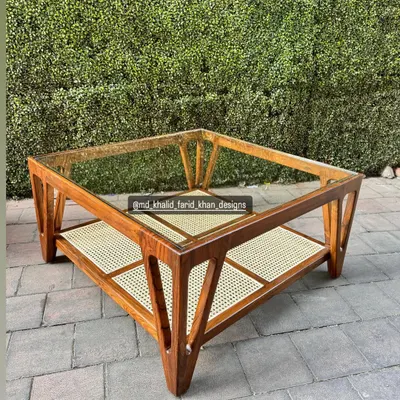 A beautiful mid-century inspired coffee table with a glass top and a lower shelf made of hand-woven cane. The angular, solid teak frame makes it a standout piece for any living room.