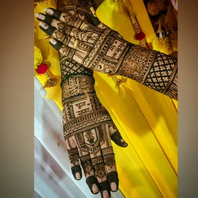 A beautiful bridal mehendi set against a vibrant yellow backdrop. This design features the couple's names, Pooja and Sagar, prominently on the palms, surrounded by traditional symbols and detailed jaali (net) patterns.