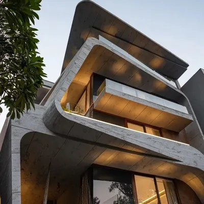 This home is a composition of cuboid and curvilinear volumes, punctuated by open balconies. The juxtaposition of sharp geometric shapes with organic forms creates a dynamic and visually engaging piece of architecture.