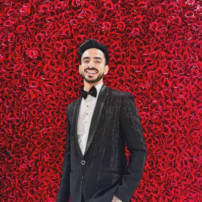A client looking sharp against a wall of red roses in our Katdana-shower work tuxedo. The subtle sparkle on the jacket makes it a perfect choice for a glamorous evening reception.