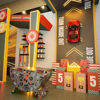 A themed game area within "Shaurya's Garage," featuring a bean bag toss and other activities designed with race car graphics and colors.