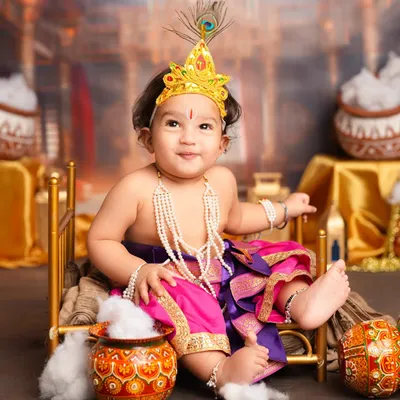 An adorable baby photoshoot celebrating Janmashtami. This little one is dressed up as Krishna, complete with a peacock feather crown and pots of butter, creating a cute and festive memory.
