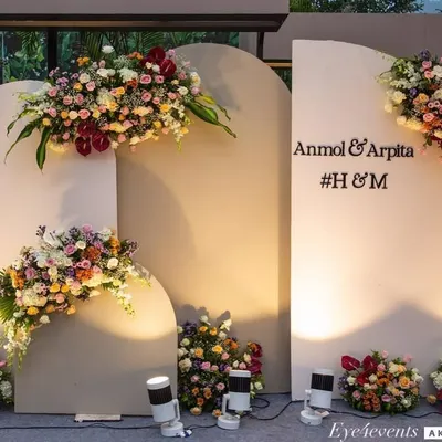 This modern and elegant photo backdrop features three arched panels in a neutral grey tone. The panels are decorated with lush, asymmetrical floral arrangements in vibrant colors and personalized with the couple's names.