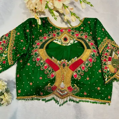 This emerald green blouse is designed for a grand bridal look. It features a dramatic back cutout, intricate kundan and zardosi work, and peacock motifs on the flared sleeves.
