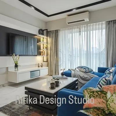 A close-up view of this modern living room highlights the contrast between the vibrant blue L-shaped sofa and the sleek black and white media unit. Sheer curtains allow for ample natural light, making the space feel bright and airy despite the bold color choices.