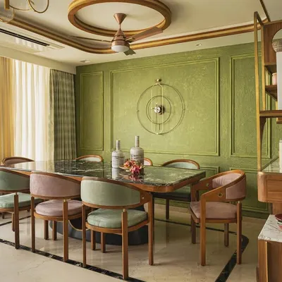 The dining space in the Melange House, where Victorian-inspired moulding on olive green walls creates a rich, textured backdrop. The custom dining table and chairs, along with the open shelving console, blend Indian craftsmanship with global design influences.