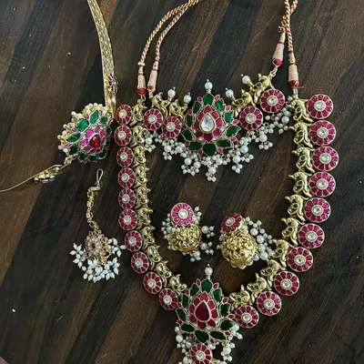 A beautiful Jadau-style set with red and green kemp stones and pearl clusters. This rental includes a choker, a longer necklace, maang tikka, and bajuband.