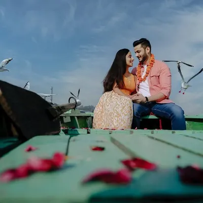 A classic Bollywood-style pre-wedding shot on a boat at Yamuna Ghat. The flock of birds, blue sky, and the couple's happy gaze create a picture-perfect romantic moment.