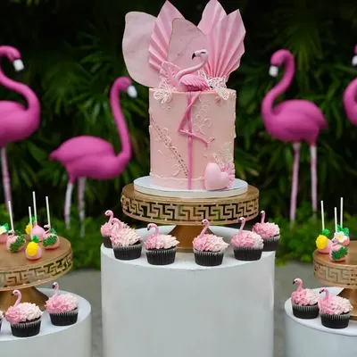 A complete Flamingo Paradise dessert table designed for a vibrant kid's birthday. The display is built around a central themed cake and includes dozens of matching pink cupcakes and cakepops on coordinated stands.