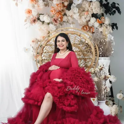 A radiant portrait of a mom-to-be in a magnificent magenta ruffled gown. Seated on a peacock chair against a wall of flowers, this shot is full of color and joy.
