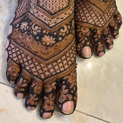 A close-up of the intricate details on this bridal feet mehendi. You can see the delicate lotus flowers and the fine lines of the checkerboard pattern on the toes.