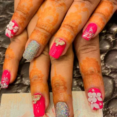 A vibrant and festive set perfect for a bride. This design combines hot pink nails, silver glitter accents, and nails with 3D sculpted flowers and bows, all complementing the henna-stained hands.